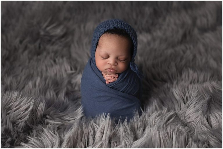 Newborn picture with navy blue jersey wrap and knitted cap with textured dark gray background. Studio located in Sierra Vista, Arizona.